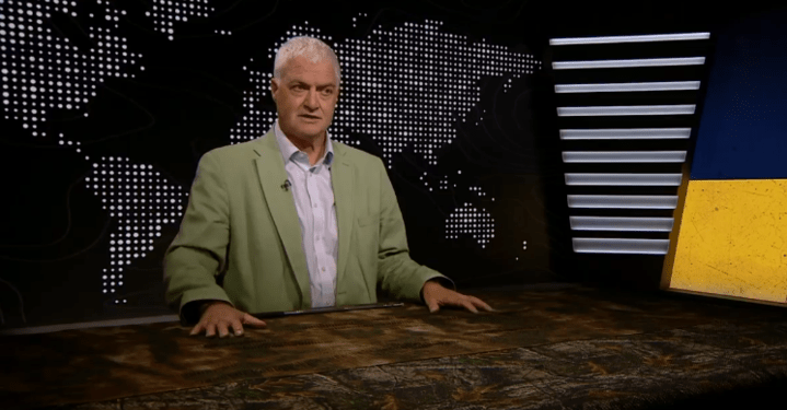El hombre con chaqueta verde se sienta en un escritorio que da una presentación frente a un mapa mundial.