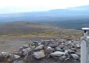 Equipo de monitoreo sísmico en una ladera rocosa con vistas a un vasto paisaje plano.