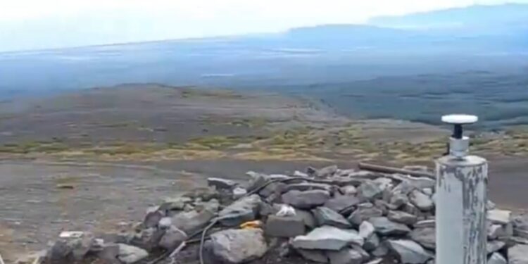 Equipo de monitoreo sísmico en una ladera rocosa con vistas a un vasto paisaje plano.