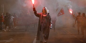 Un manifestante con un traje protector y casco plateado tiene una llamarada iluminada en Marsella, Francia, durante una protesta a nivel nacional.