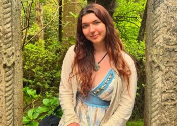 Rebecca McCurry, de 22 años, posando al aire libre con un vestido con un cárdigan blanco.