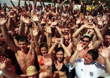 Gran grupo de jóvenes en una fiesta en la piscina, levantando las manos.