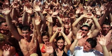 Gran grupo de jóvenes en una fiesta en la piscina, levantando las manos.