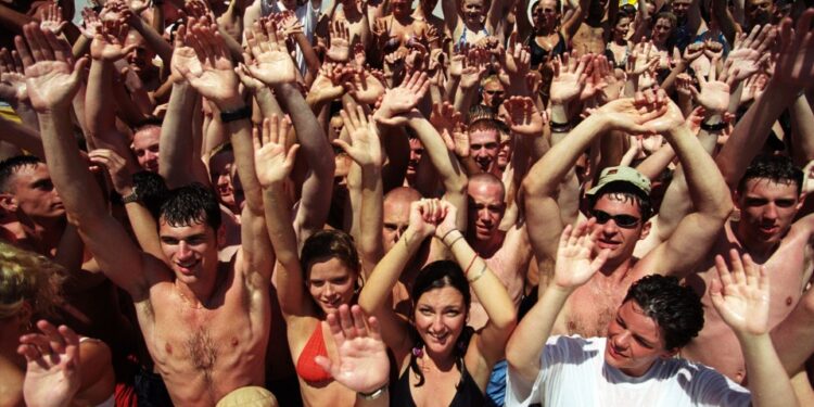 Gran grupo de jóvenes en una fiesta en la piscina, levantando las manos.