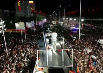 Un político se dirige a una gran multitud desde una plataforma en un escenario por la noche.