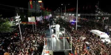 Un político se dirige a una gran multitud desde una plataforma en un escenario por la noche.