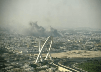 Vista aérea de una ciudad con un gran penacho de humo negro y un puente moderno.