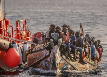 Los migrantes rescatados en un pequeño bote son remolcados por un barco  grande.