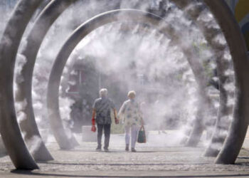 Una pareja se enfría mientras caminan a través de una función de agua de enfriamiento rociando una fina niebla en Dover, Kent, cuando la tercera ola de calor del verano llega al Reino Unido y se espera que se mantengan altas en el fin de semana, el 11 de julio de 2025.