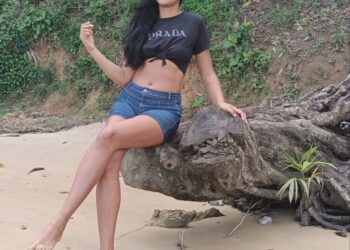 Mujer sentada en un registro en una playa de arena.