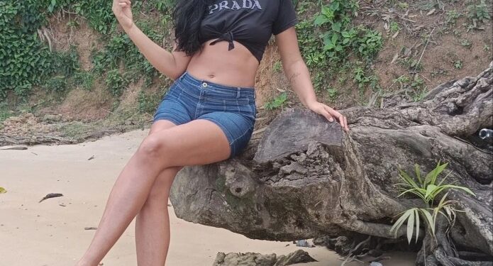 Mujer sentada en un registro en una playa de arena.