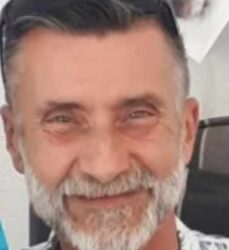 Un hombre con barba gris y gafas de sol en la cabeza sonriendo ligeramente.