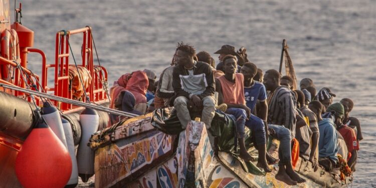 Los migrantes en un bote colorido son asistidos por un recipiente de búsqueda y rescate en español rojo en el mar.