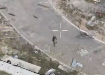 Una mira dirigida a una persona en una calle en un asentamiento devastado por la guerra.