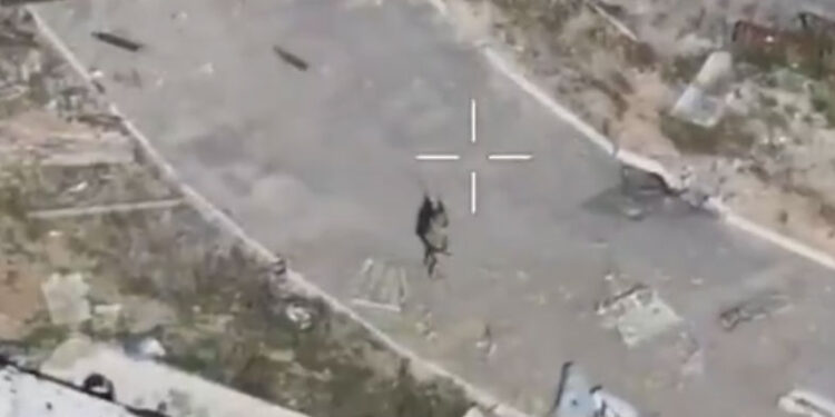 Una mira dirigida a una persona en una calle en un asentamiento devastado por la guerra.