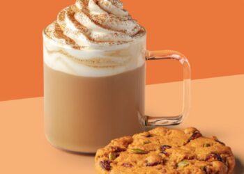 Un café con leche de especias de calabaza Starbucks con crema batida y una galleta con arándanos y semillas de calabaza.