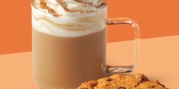 Un café con leche de especias de calabaza Starbucks con crema batida y una galleta con arándanos y semillas de calabaza.
