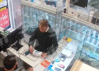 Las imágenes de CCTV muestran a un hombre con una sudadera con capucha negra que compraba un teléfono en un mostrador en una tienda.