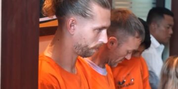 Dos hombres británicos con monos de naranja en una conferencia de prensa después de su arresto por presuntamente contrabando de cocaína.