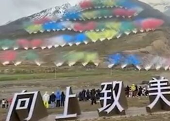 Se exhiben fuegos artificiales con múltiples columnas de humo coloridas en una montaña, sobre grandes caracteres chinos blancos.