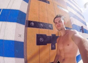 Hombre sin camisa tomando una selfie frente a un mural.