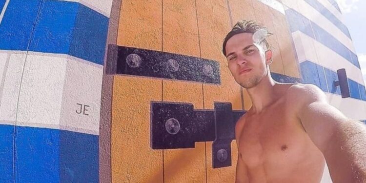 Hombre sin camisa tomando una selfie frente a un mural.