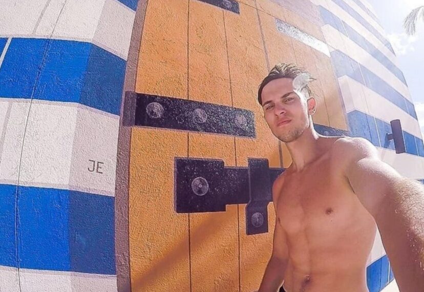 Hombre sin camisa tomando una selfie frente a un mural.