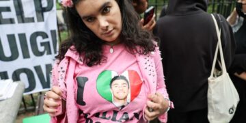 Un partidario de Luigi Mangione con un "Amo a los chicos italianos" camisa con una foto de un hombre en el corazón de la bandera italiana, con un "Ayuda a Luigi" firmar en el fondo.
