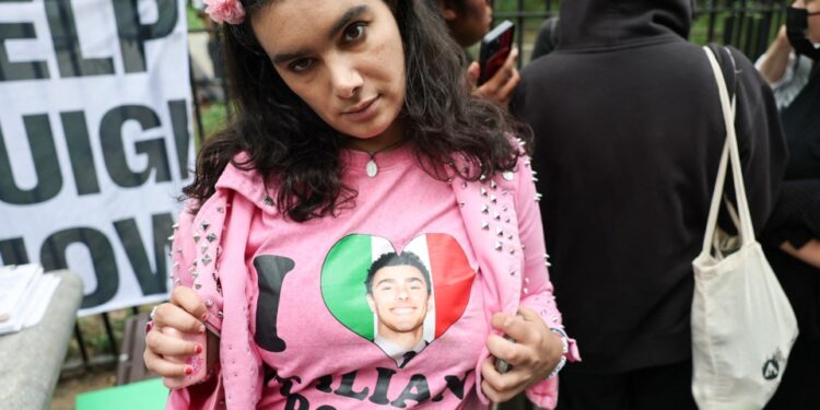 Un partidario de Luigi Mangione con un "Amo a los chicos italianos" camisa con una foto de un hombre en el corazón de la bandera italiana, con un "Ayuda a Luigi" firmar en el fondo.