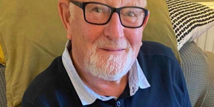 Clifford Wildgoose, un abuelo británico, sentado con gafas con marco negro y barba blanca.