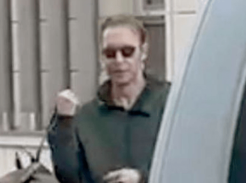 Hombre con gafas de sol y una sudadera oscura, con su mano izquierda apretada.