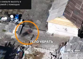 Las imágenes aéreas muestran un cuerpo humano borrosa que se encuentra en el suelo al lado de un pequeño edificio, con un círculo naranja que lo resalta, y textan en la superposición rusa de la imagen.