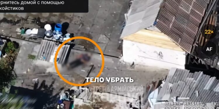 Las imágenes aéreas muestran un cuerpo humano borrosa que se encuentra en el suelo al lado de un pequeño edificio, con un círculo naranja que lo resalta, y textan en la superposición rusa de la imagen.