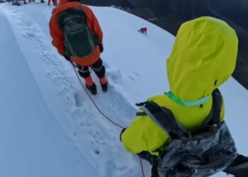Los excursionistas en una cresta de montaña nevada con un pico en el fondo.
