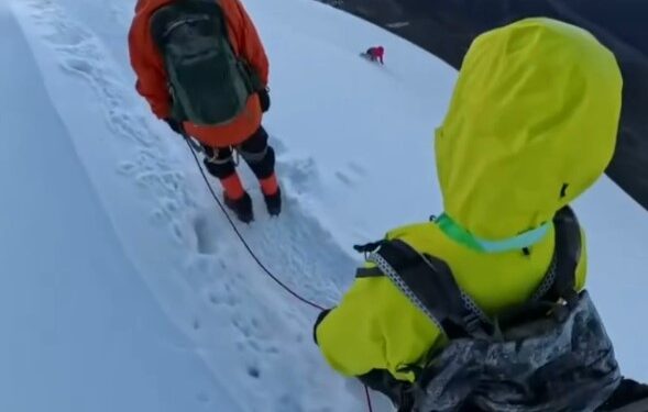 Los excursionistas en una cresta de montaña nevada con un pico en el fondo.