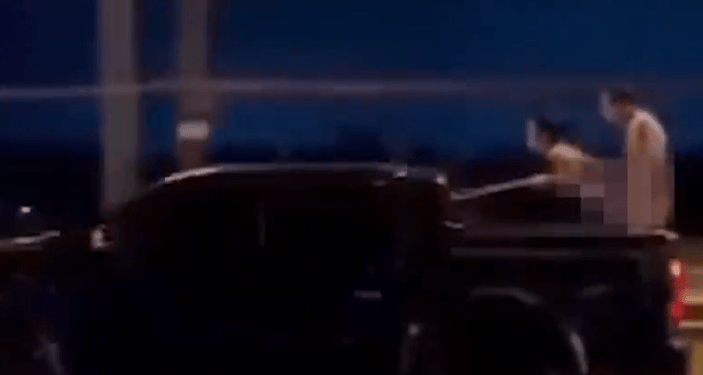 Dos personas con cuerpos borrosos en la cama de un camión en movimiento.