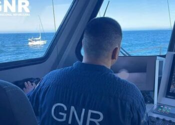 Oficial de GNR en la cabina de un bote, mirando un velero en el océano.
