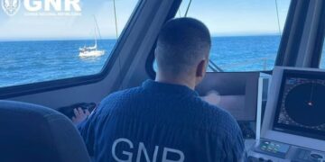 Oficial de GNR en la cabina de un bote, mirando un velero en el océano.