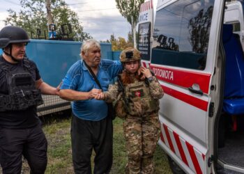 Los oficiales de policía ayudan a un anciano a transferirse de un automóvil blindado a una ambulancia.