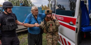 Los oficiales de policía ayudan a un anciano a transferirse de un automóvil blindado a una ambulancia.