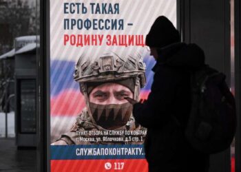 Persona en una parada de autobús mirando una pantalla publicitaria que promueve el servicio militar contractual en el ejército ruso.