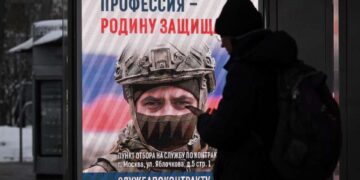 Persona en una parada de autobús mirando una pantalla publicitaria que promueve el servicio militar contractual en el ejército ruso.