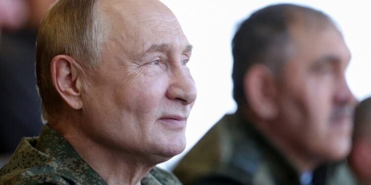 El presidente ruso, Vladimir Putin, con un uniforme militar, mirando hacia la derecha, con otro hombre borroso en el fondo.