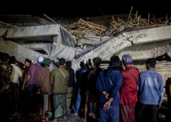 Parientes parados frente a un edificio colapsado durante una operación de rescate en un internado islámico.