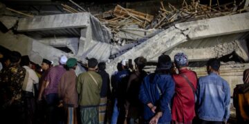 Parientes parados frente a un edificio colapsado durante una operación de rescate en un internado islámico.