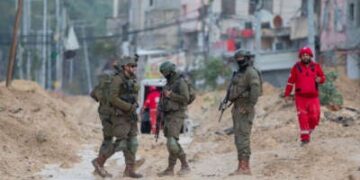 Los soldados israelíes caminan por una calle fangosa mientras un trabajador humanitario camina en el campamento de refugiados de Nur Shams en Cisjordania, Palestina, el 10 de febrero de 2025.