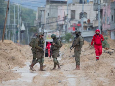 Los soldados israelíes caminan por una calle fangosa mientras un trabajador humanitario camina en el campamento de refugiados de Nur Shams en Cisjordania, Palestina, el 10 de febrero de 2025.