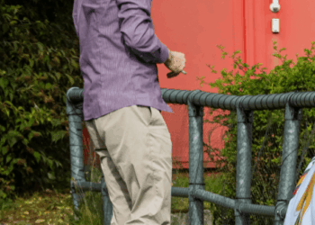 Un hombre con una camisa a rayas y pantalones de color caqui camina con un monitor de tobillo en la pierna.