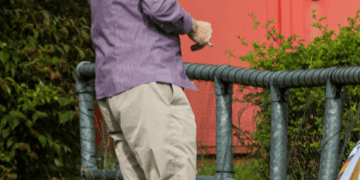 Un hombre con una camisa a rayas y pantalones de color caqui camina con un monitor de tobillo en la pierna.