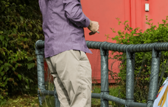 Un hombre con una camisa a rayas y pantalones de color caqui camina con un monitor de tobillo en la pierna.
